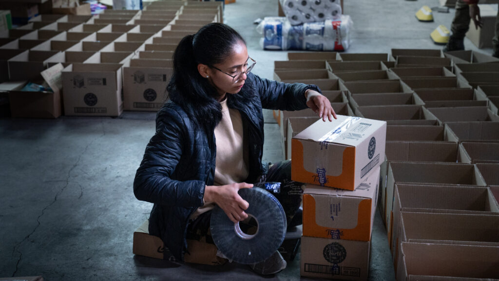 Voluntaria sellando cajas de ayuda con cinta en la bodega