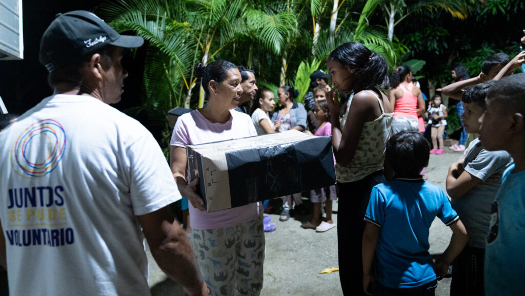 Familia recibiendo una caja de ayuda de manos de un voluntario en la noche